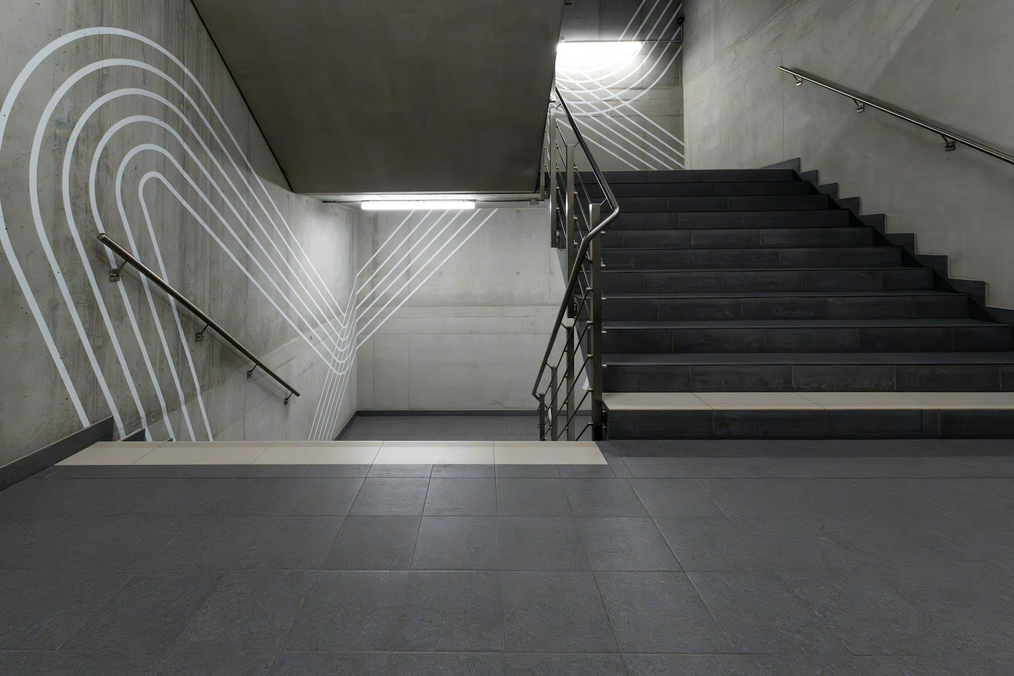 Concrete stairwell with a graphic steel handrail and wall markings